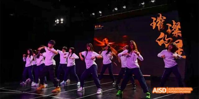 A group of students from HAIDE Bilingual School Dongguan performing a dance routine on a stage with purple lighting.
