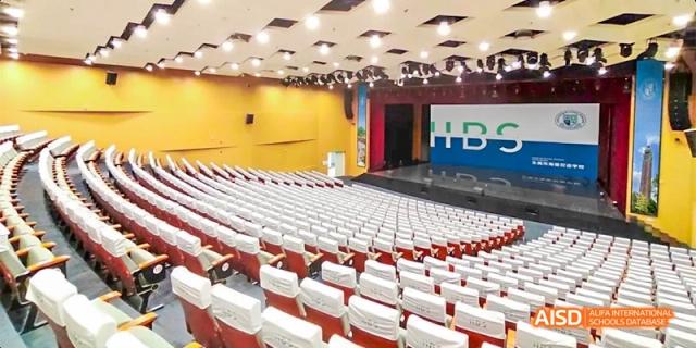 The empty auditorium at HAIDE Bilingual School Dongguan, showing rows of white seats and a stage with yellow and blue walls.