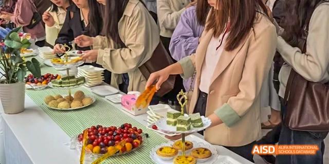 A close-up shot of hands reaching for various desserts and fruits on a plate at a catered event at HAIDE Bilingual School Dongguan.
