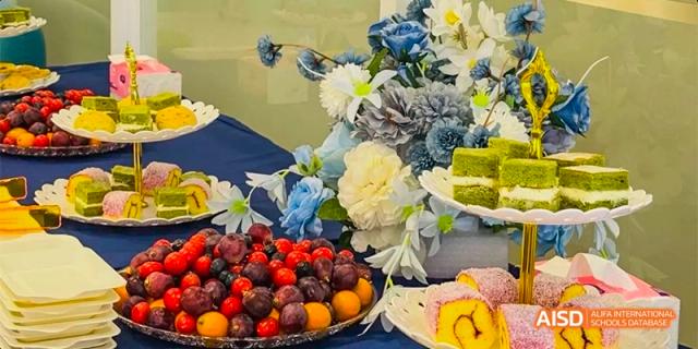A close-up shot of a table with a flower arrangement and various fruits, cakes, and other desserts at an event at HAIDE Bilingual School Dongguan.