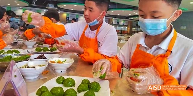 Food service workers from HAIDE Bilingual School Dongguan wearing orange aprons and hairnets while preparing food for students.
