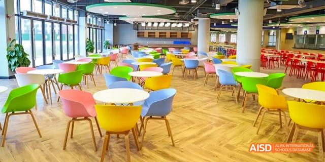 The bright, colorful, and modern cafeteria at HAIDE Bilingual School Dongguan, with yellow and blue chairs around tables.