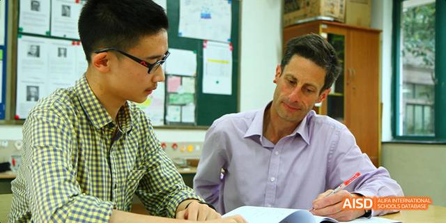 A teacher and a student from Hangzhou Foreign Languages School having a one-on-one discussion or tutoring session in a classroom setting.