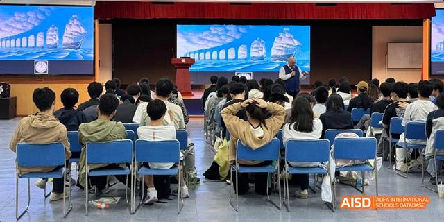 Students from Hangzhou Foreign Languages School seated in an assembly hall, watching a presentation projected onto a large screen showing a bridge structure.