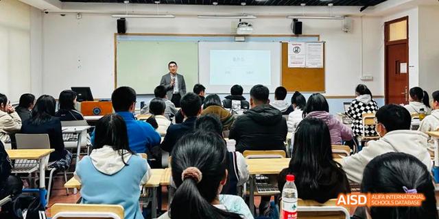 A teacher lecturing a large class of seated students in a Hangzhou Foreign Languages School classroom, viewed from the back of the room.