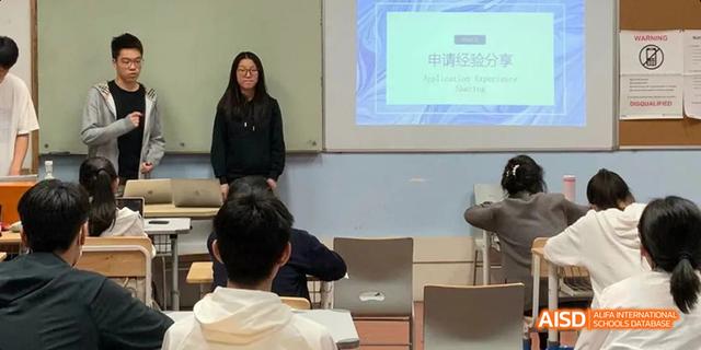 A female student from Hangzhou Foreign Languages School giving a presentation in front of her class, standing next to a projected slide on the screen.