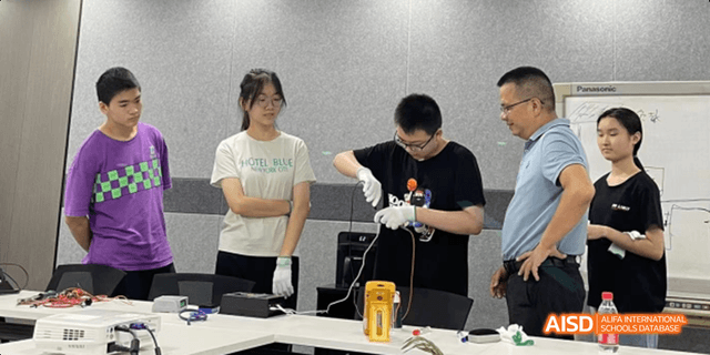 A female Hangzhou Foreign Languages School student observing a male student performing a detailed procedure or experiment on a table in a lab or classroom.