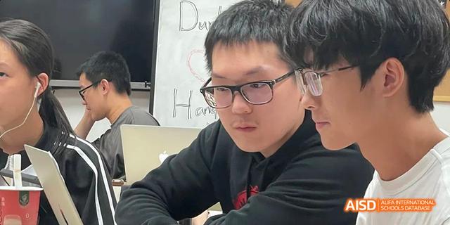 A close-up portrait of a male Hangzhou Foreign Languages School student wearing glasses, looking intently at something off-camera during a class or workshop.