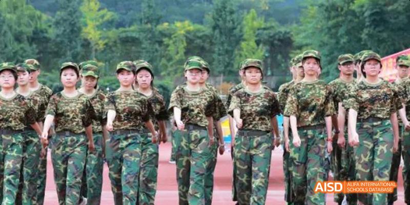 Hangzhou Foreign Languages School students marching in camouflage uniforms during a military training exercise, with a background of green trees.