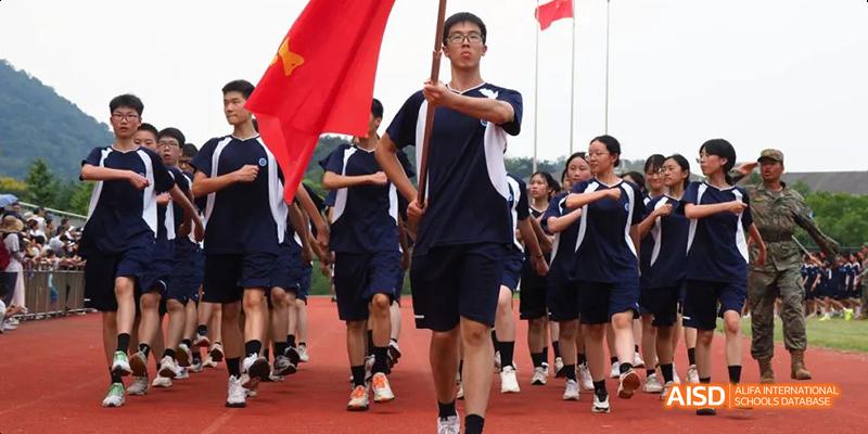 A group of Hangzhou Foreign Languages School students in dark blue uniforms jogging or marching together, possibly as part of a sports day parade.