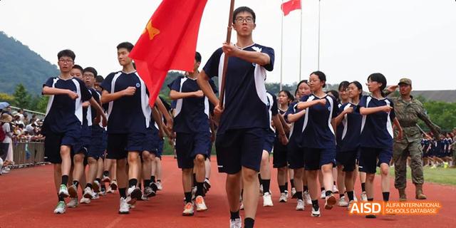 A group of Hangzhou Foreign Languages School students in dark blue uniforms jogging or marching together, possibly as part of a sports day parade.