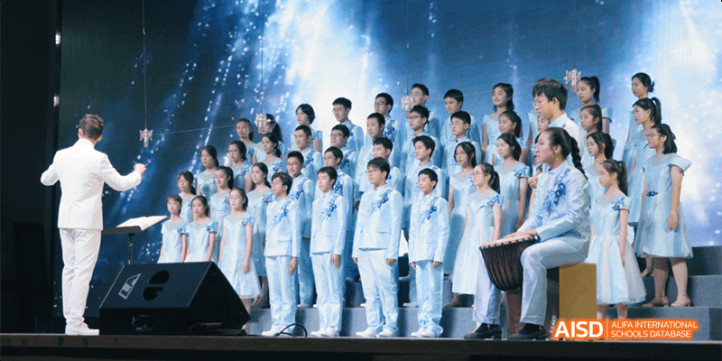 A large choir or performance group of Hangzhou Foreign Languages School students, all dressed in matching light blue uniforms, performing on a stage.