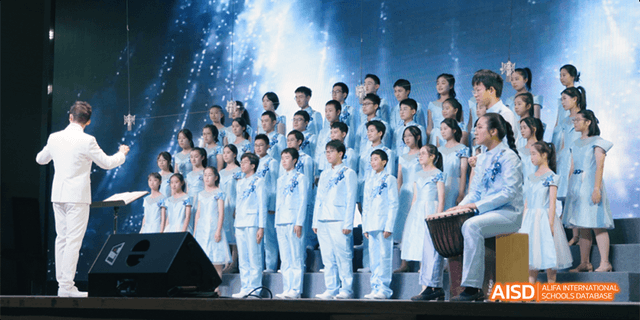 A large choir or performance group of Hangzhou Foreign Languages School students, all dressed in matching light blue uniforms, performing on a stage.