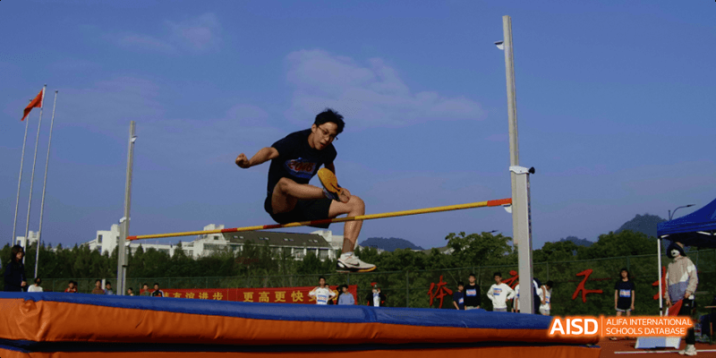 A Hangzhou Foreign Languages School student successfully clearing the bar during a high jump competition, outdoors on the school field.