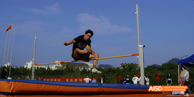 A Hangzhou Foreign Languages School student successfully clearing the bar during a high jump competition, outdoors on the school field.
