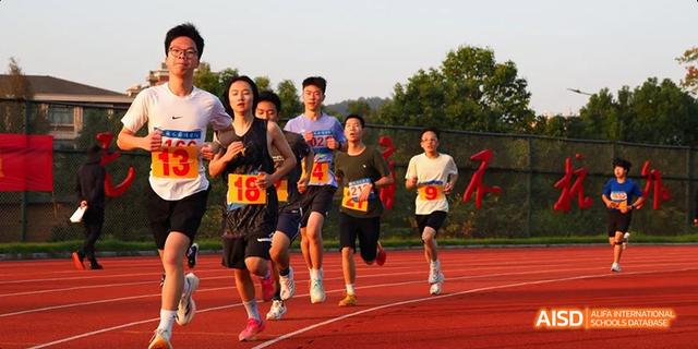 Hangzhou Foreign Languages School students wearing numbered bibs competing in a middle-distance running race on the track during a sports meet.