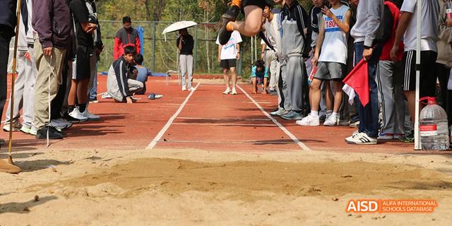 Close-up shot of a long jump pit and the red running track, showing Hangzhou Foreign Languages School students preparing to compete in a field event.