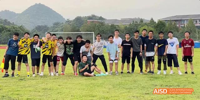 A large group of Hangzhou Foreign Languages School students posing together for a casual photo on a grassy field with hills in the background.
