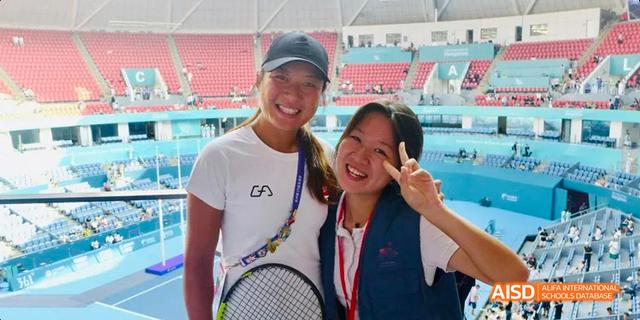 Two smiling female students from Hangzhou Foreign Languages School taking a selfie, wearing sports attire and holding a tennis racket, likely after a competition.