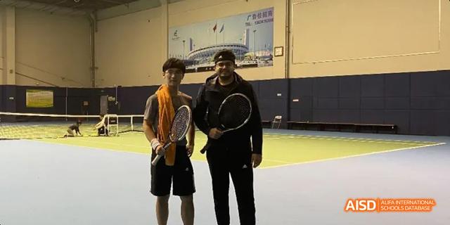 Two individuals, possibly a teacher and a student from Hangzhou Foreign Languages School, posing on an indoor court while holding tennis rackets.