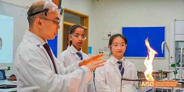A female student from Harrow LiDe School Haikou in a lab coat is smiling and holding a beaker in a science lab.