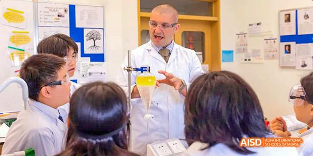 A male teacher from Harrow LiDe School Haikou in a lab coat is demonstrating a science experiment to students.