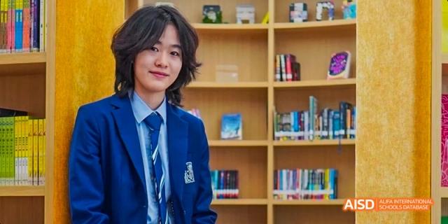 A female student from Harrow LiDe School Haikou is smiling while holding a book in a library.