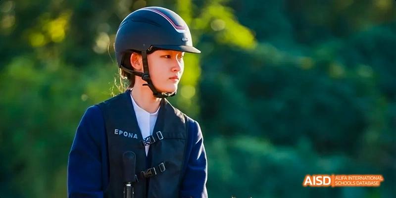 A male student from Harrow LiDe School Haikou wears a helmet and riding vest, likely for an equestrian or outdoor activity.