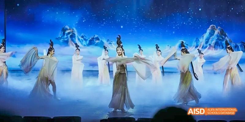 A female student from Harrow LiDe School Haikou performs a traditional Chinese dance on a stage with a starry night backdrop.