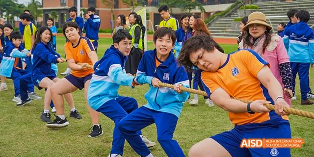 A group of students from Harrow LiDe School Haikou competes in a tug-of-war game on a grassy field.