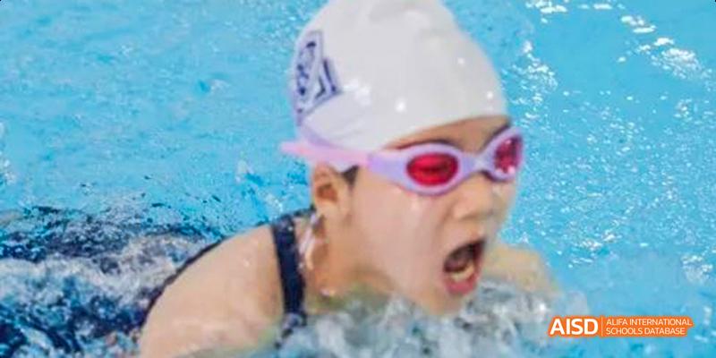 A female swimmer from Harrow LiDe School Haikou with goggles is seen mid-stroke.