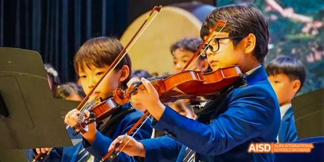 A group of students from Harrow LiDe School Haikou are playing instruments in an orchestra, with one student in the foreground playing a violin.