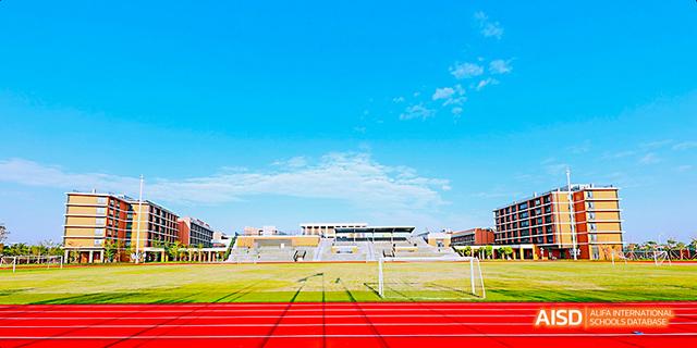 A view of a sports field and track on the campus of Harrow LiDe School Haikou under a blue sky.
