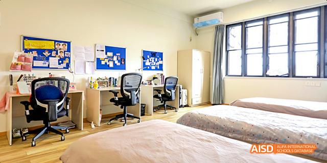 A student dormitory room at Harrow LiDe School Haikou, featuring a bed, a desk, and a chair.
