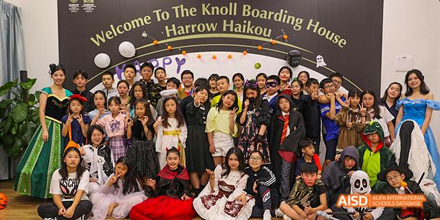 A group of students from Harrow LiDe School Haikou pose together for a group photo in front of a banner that reads "The Knoll Boarding Harrow Haikou".