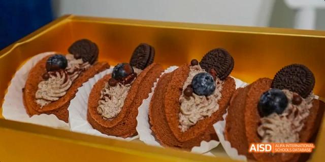 A chocolate Swiss roll with whipped cream and berries, part of a dessert spread at Harrow LiDe School Haikou.