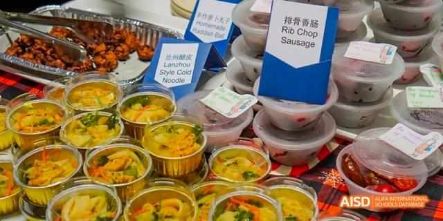 A stand with bowls of noodles and other food items, labeled in both Chinese and English, at an event at Harrow LiDe School Haikou.