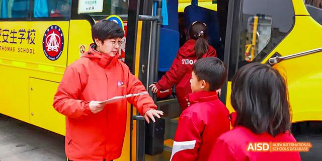 Students in red jackets boarding a yellow school bus with assistance from a staff member at Hefei Thomas School.