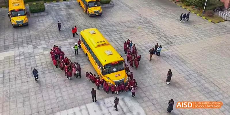 An aerial view of a group of students and staff waiting outside a yellow school bus at Hefei Thomas School.