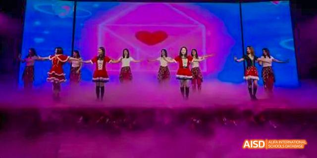 Hefei Thomas School students performing a modern dance routine on a stage with vibrant pink and purple lighting.