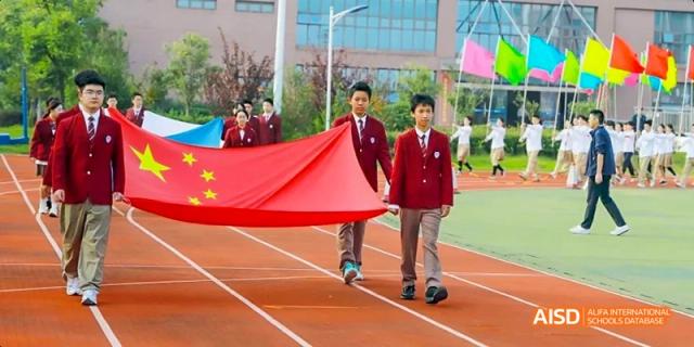 Hefei Thomas School students running on a track while holding a large red banner.