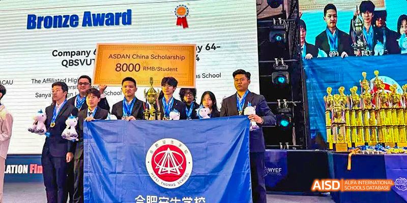 Hefei Thomas School students and a teacher posing for a group photo with awards and a school banner.