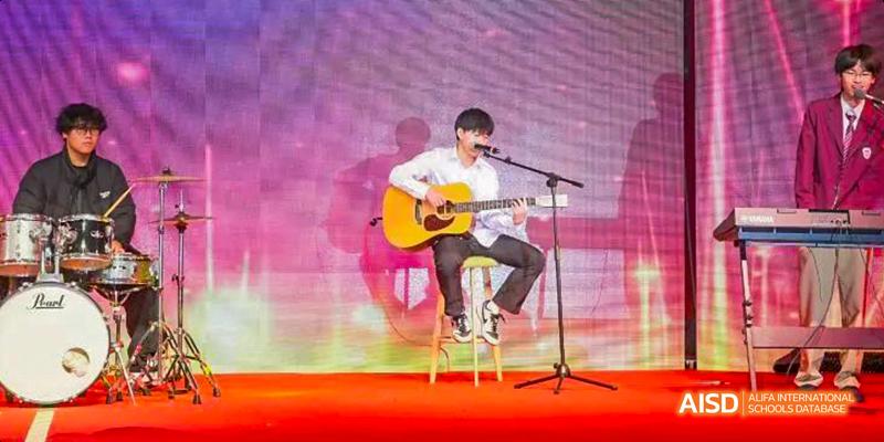 Hefei Thomas School student playing an acoustic guitar and singing on a stage.