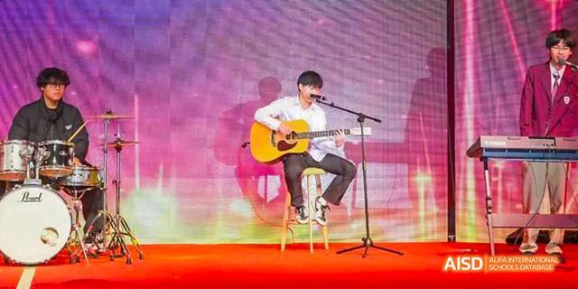 Hefei Thomas School student playing an acoustic guitar and singing on a stage.