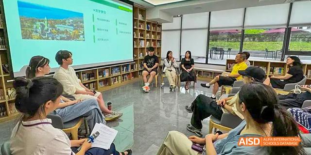 A small group of students from the International Department of Chengdu Shude High School attending a lecture or meeting in a relaxed setting, with a screen in the background.