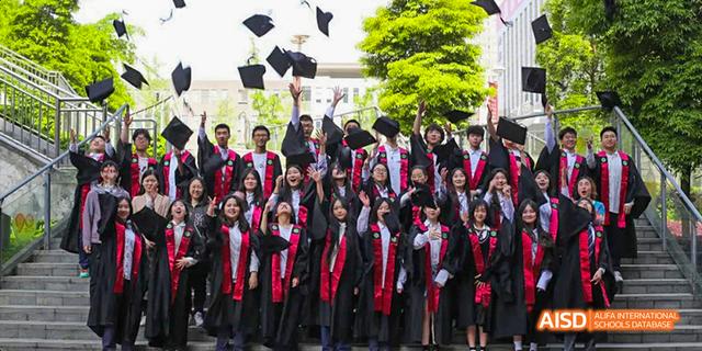 A large group of graduating students from the International Department of Chengdu Shude High School in black and red graduation gowns, tossing their caps in the air outdoors.