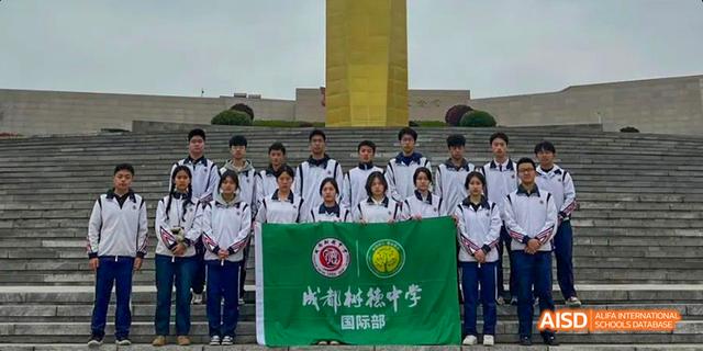 A group of students from the International Department of Chengdu Shude High School standing in uniform in front of a monument, holding the school banner.