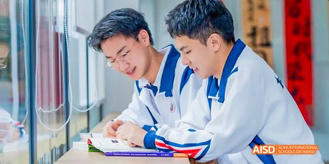 Two male students from the International Department of Chengdu Shude High School studying together, looking at a textbook and discussing their work.