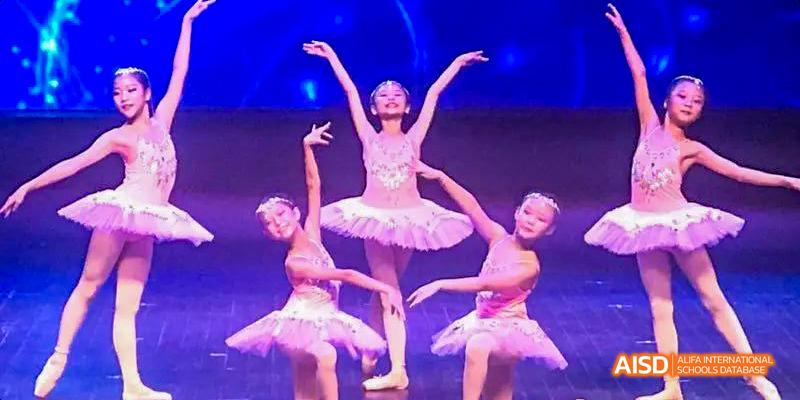 Ballet performance by students from the International Department of Chengdu Shude High School, featuring three dancers in light pink tutus on a stage.