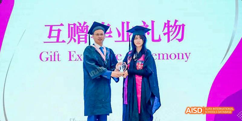 Graduation ceremony at the International Department of Chengdu Shude High School, showing a faculty member presenting an award to a student in a graduation cap and gown.